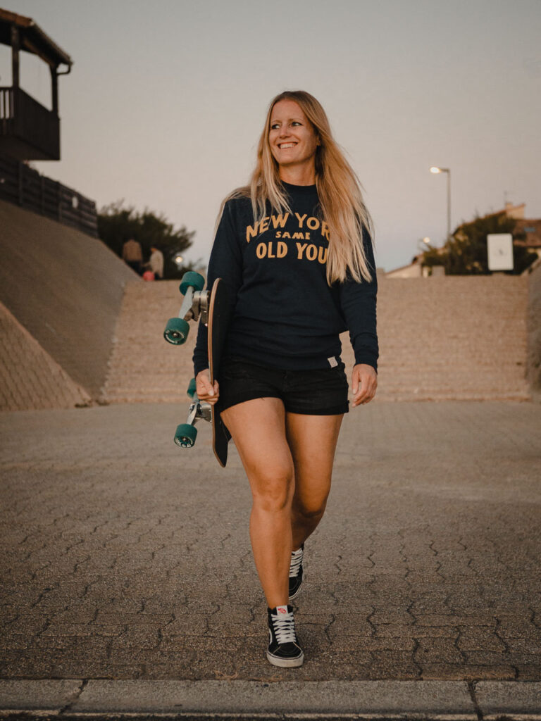 Beautiful Girl walking and smiling with her Carver Surf Skate tucked under the arm in Capbreton - France by Ondrej Kolacek