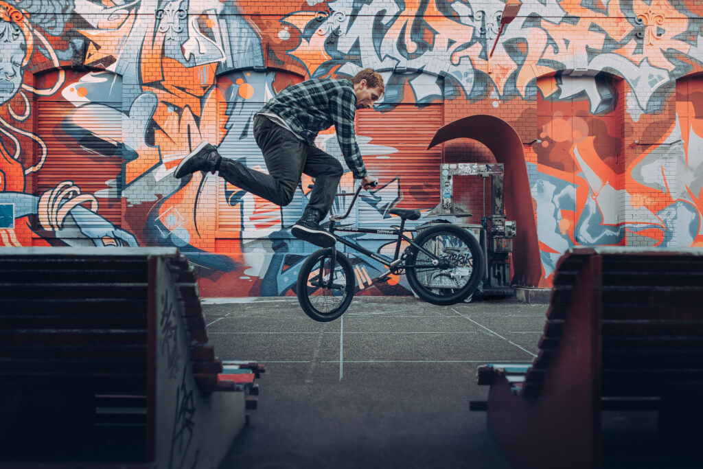 Enviromental portrait of Dan Henning, professional bmx flatland rider at Rote Fabrik with colorful graffitis on the backwall - Zurich, Switzerland by Ondrej Kolacek