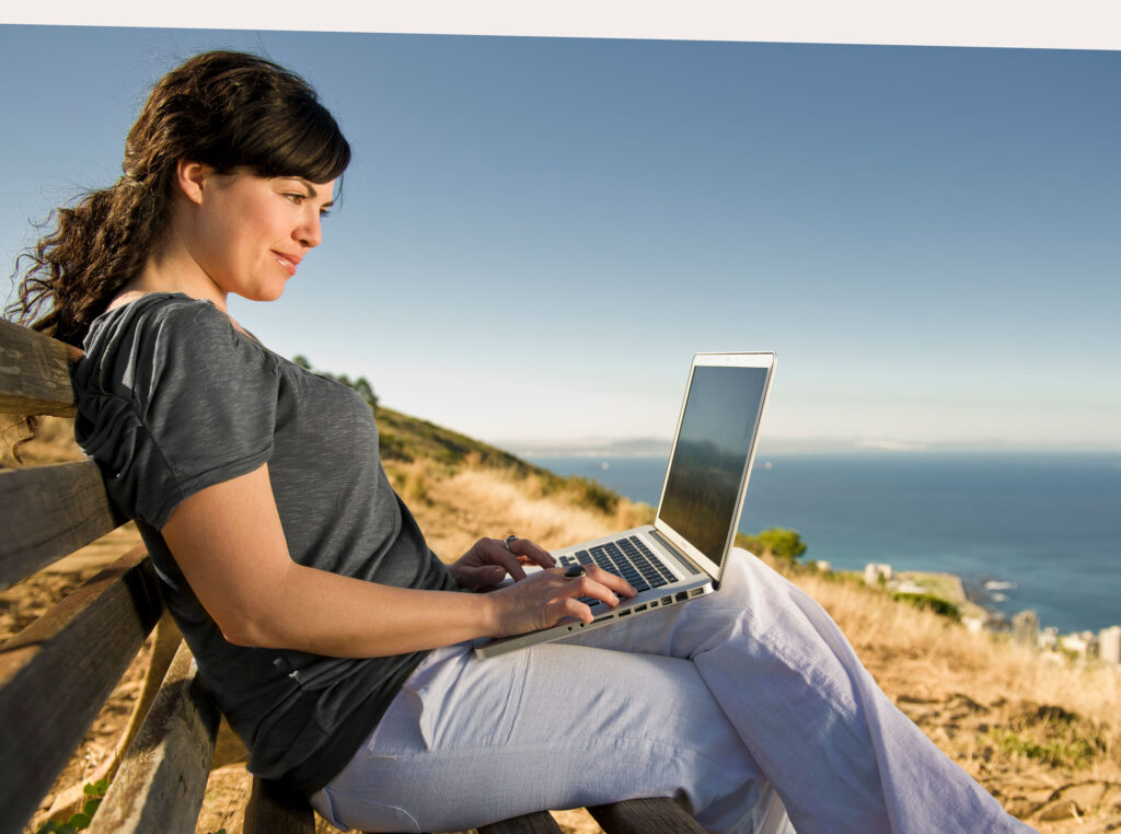 Girl sitting with her MacBook at the beach unretouched